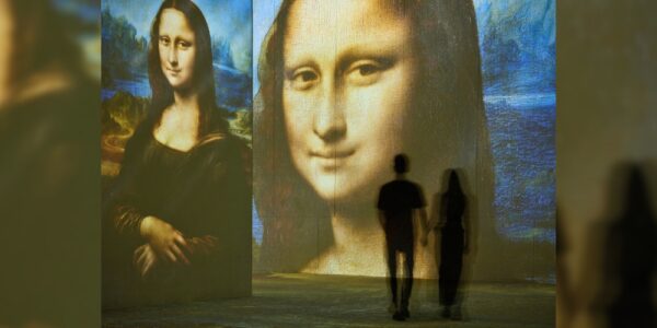 Two people standing in front of a digitally projected image of the Mona Lisa, which is part of the Leonardo di Vinci exhibit at THEMSUEM in Kitchener.