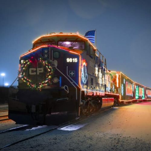 The decorated engine and cars of the CKPC Holiday Train as it travels, lit up by colourful lights, at night.