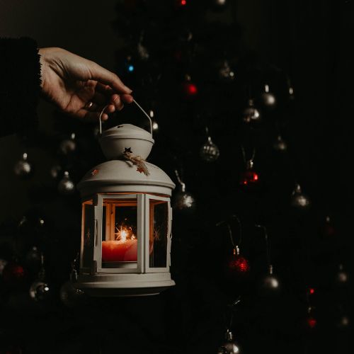 Close up of a person holding a lit lantern on a winter's night. You can see sparkly little lights in the background.