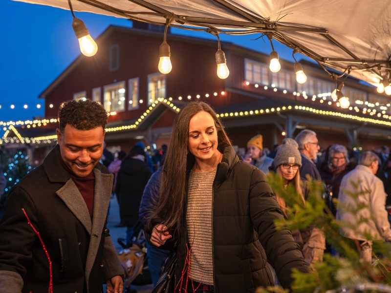 A couple is looking at the items at an outdoor vendor stall at the Holiday Sip n Shop evening event at the St. Jacobs Farmers' Market.