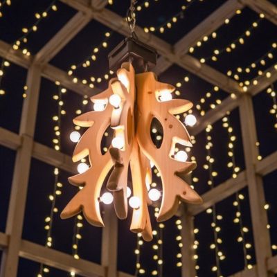 The large wooden mistletoe sculpture created by artist Sklyer Dietze, hanging in the Downtown Kitchener Light box. It is night, and both the light box and the mistletoe are lit up with white lights.