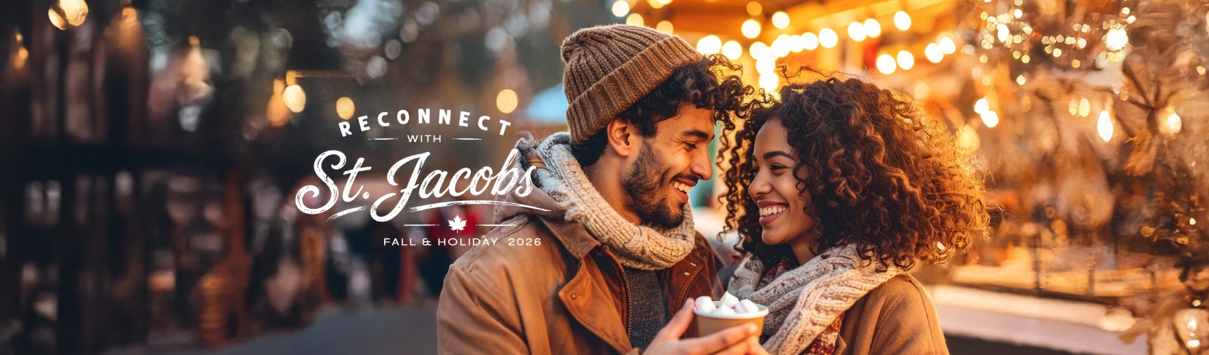A couple standing close together and smiling in the middle of a small town downtown. It is winter: the couple are both holding a cup of hot chocolate and are dressed in winter coats and toques. There are twinkling lights on the shop windows in the background. A logo on the image says Reconnect with St. Jacobs.