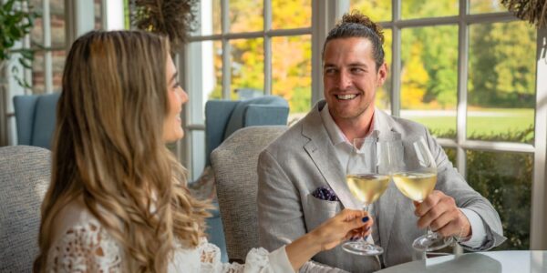 A couple sitting at a window table in the restaurant at Langdon Hall in Cambridge. They are clinking their wine glasses. It is a sunny fall day outside
